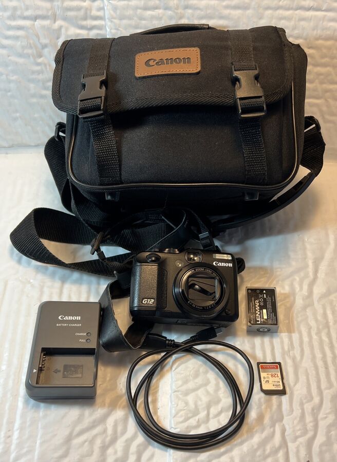 Canon PowerShot G12 black compact digital camera bundle photographed with black Canon carrying case, strap, removable battery, battery charger, cable, and memory cards